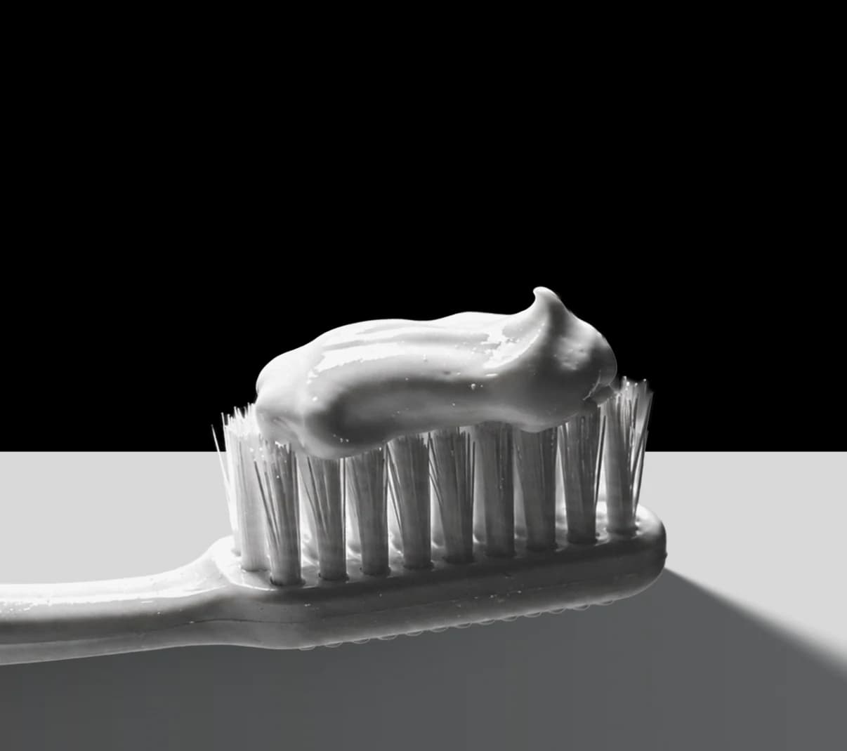 A toothbrush loaded with toothpaste, lit from the side